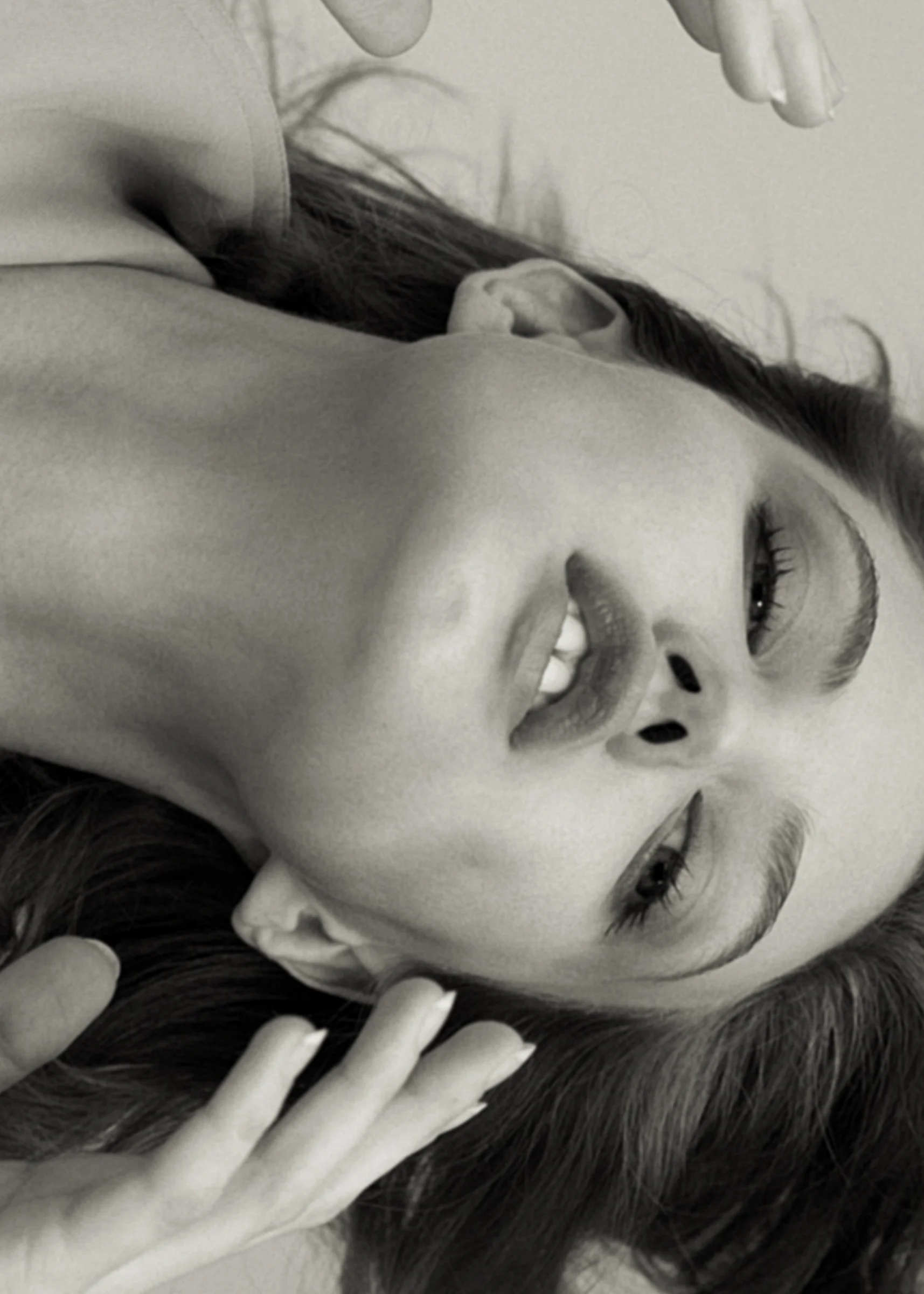 Black-and-white portrait of a woman lying back, hands in her hair