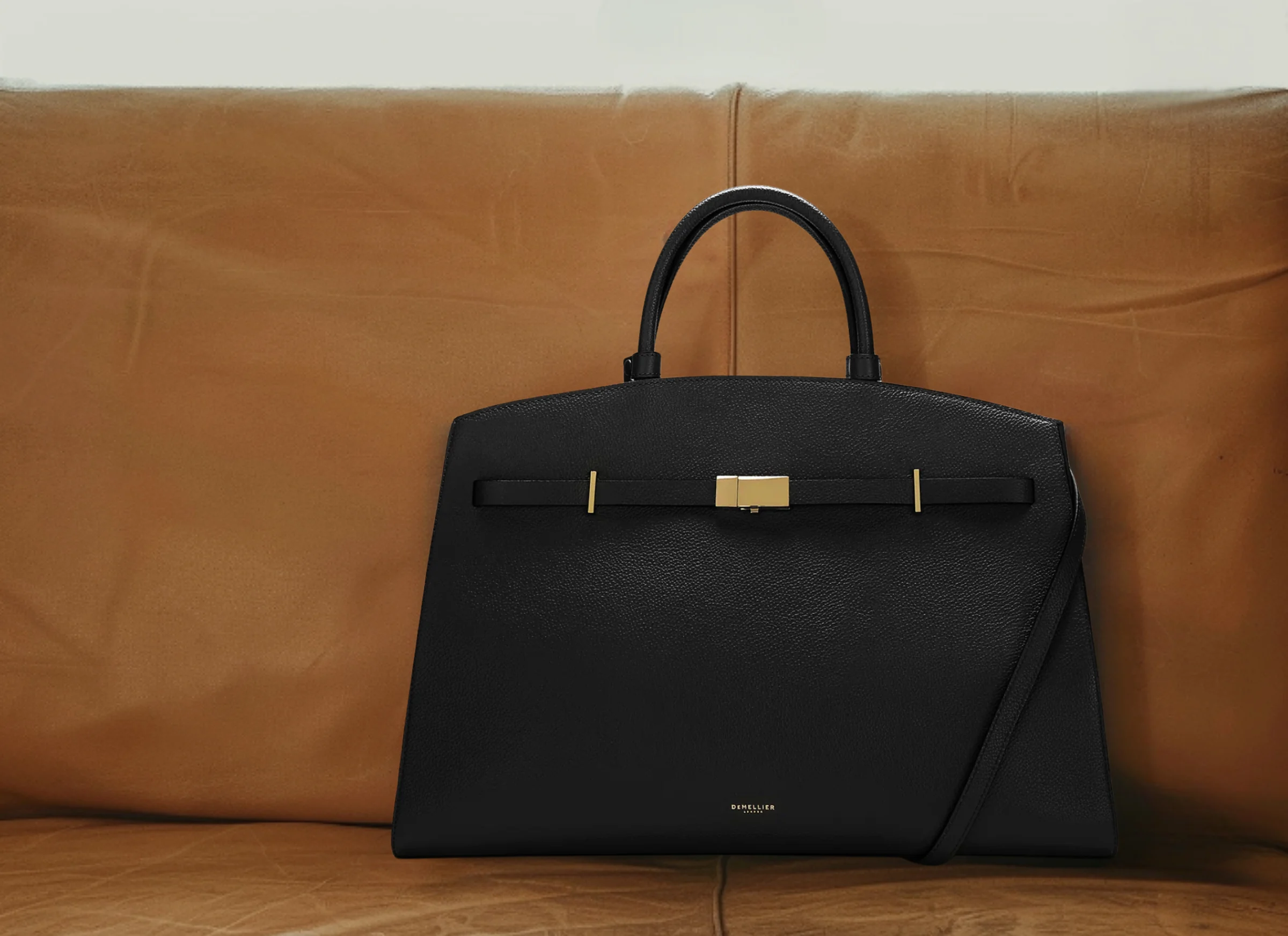 A black leather handbag on a tan sofa