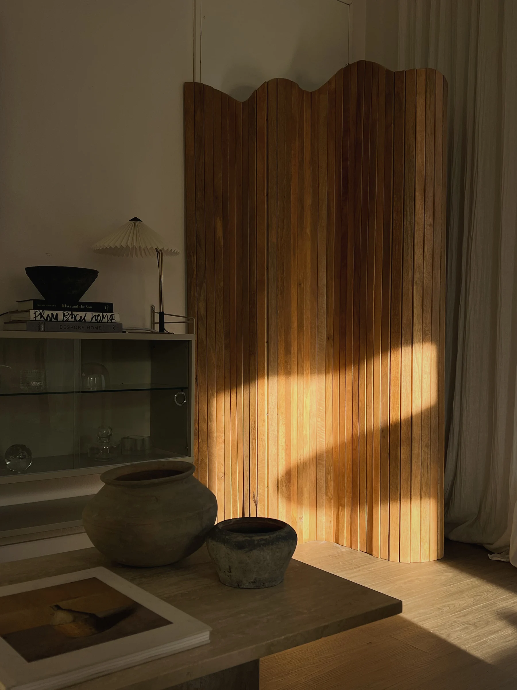 A wooden screen and stoneware in a sunlit interior