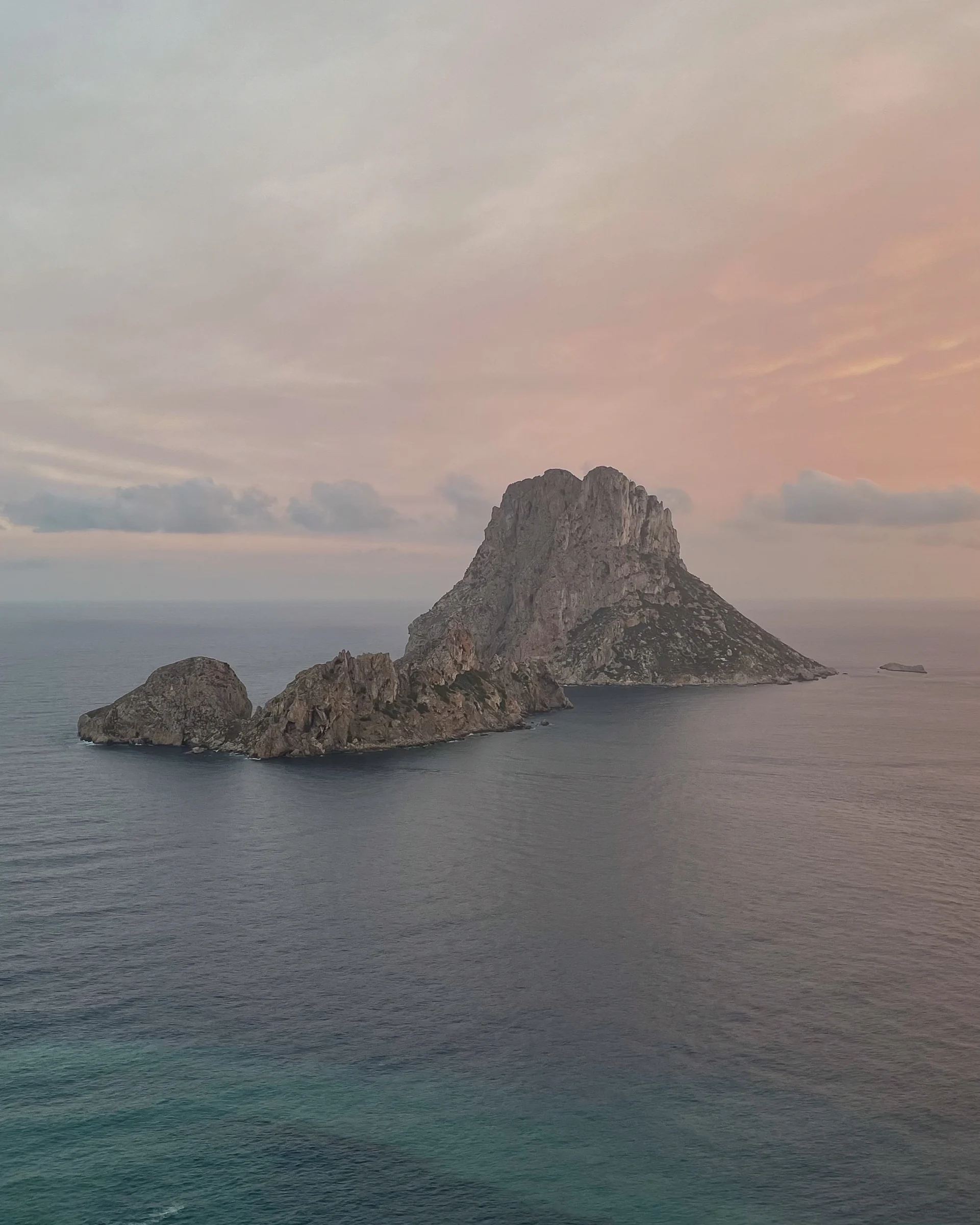 A rocky island in a calm sea at dusk